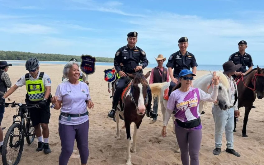 Tourist police officers and volunteers pose with horses and bicycles on a beach.