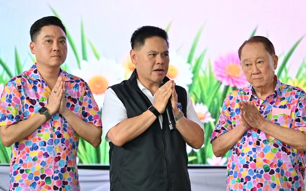 Three men stand onstage with hands clasped in a celebratory setting.