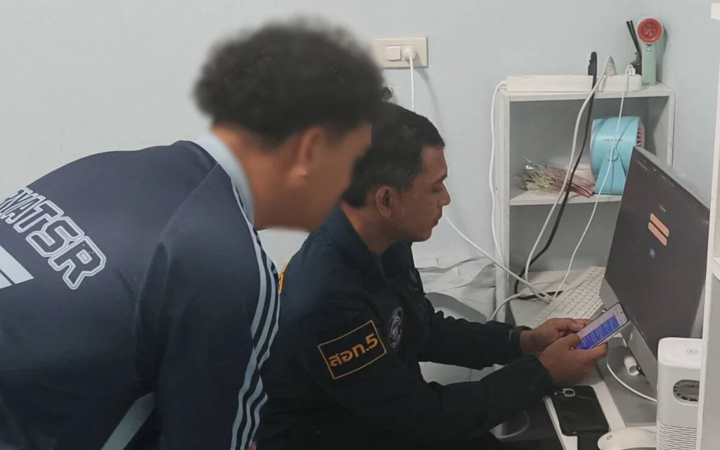 Two men examine a mobile phone beside a computer in an office.