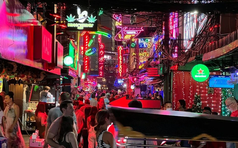 Crowded Bangkok nightlife street with neon signs and pedestrians.