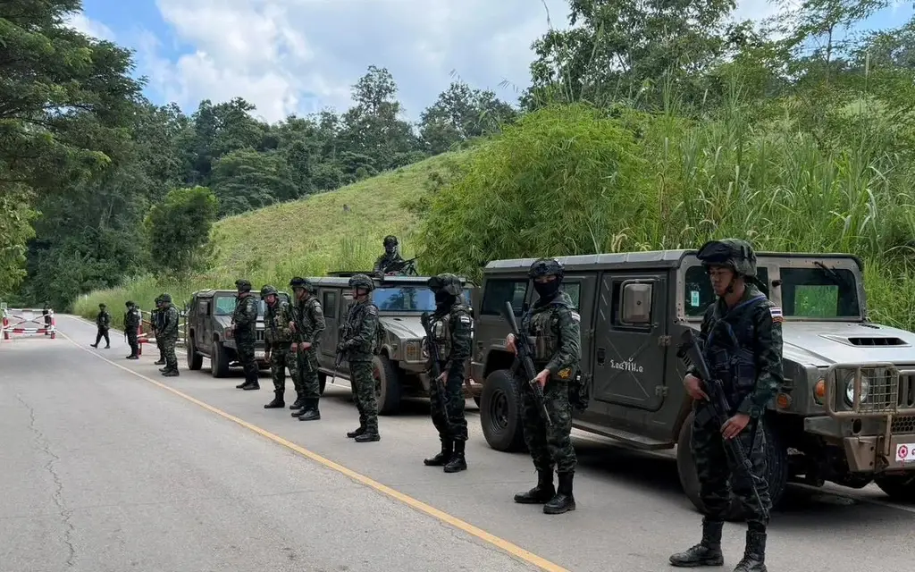 Armed soldiers stand beside military vehicles on a rural road.