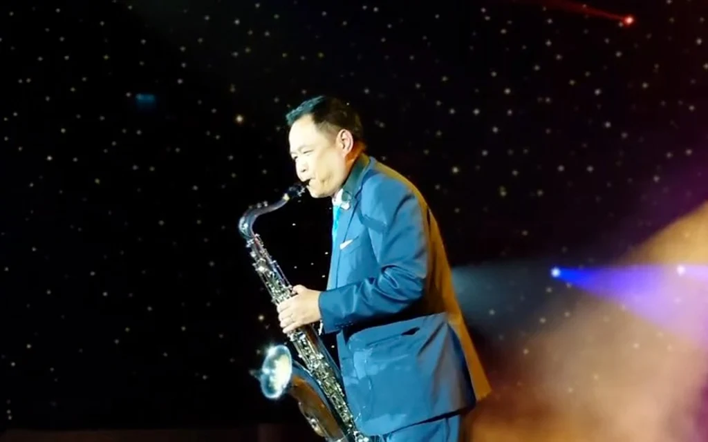 A man in a blue suit plays saxophone on a stage.