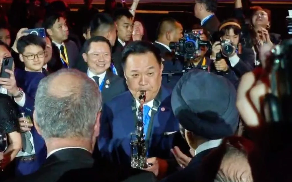Anutin plays saxophone in a crowded reception surrounded by photographers and guests.