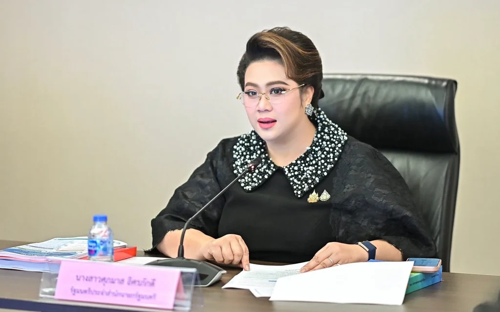 A woman speaks at a meeting table with papers and a microphone.