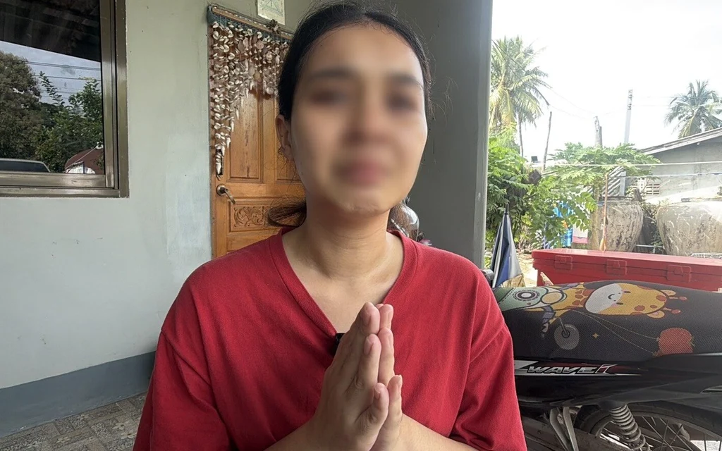 A woman in a red shirt with hands pressed together.