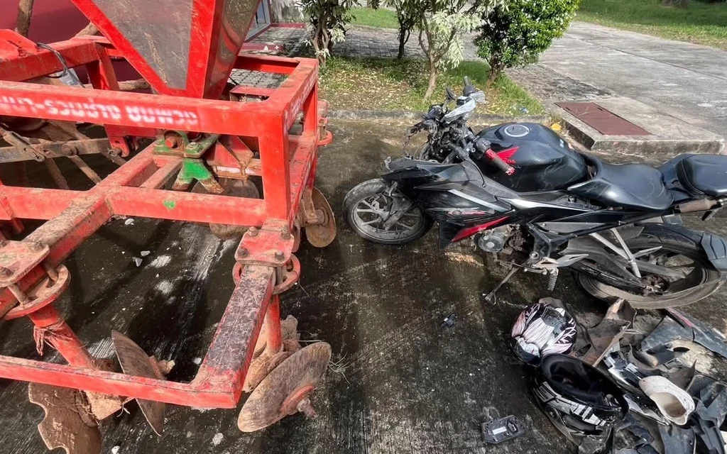A damaged motorcycle parked next to red agricultural machinery.