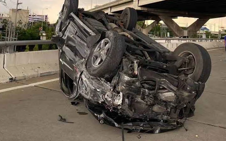 An overturned, badly damaged car on a road beneath an elevated highway.
