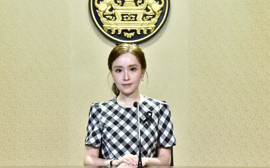 A woman sitting at a desk in front of a government emblem.