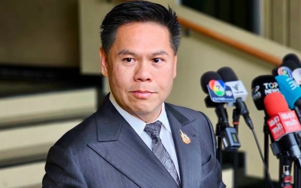 A suited man speaks to reporters beside a cluster of microphones.