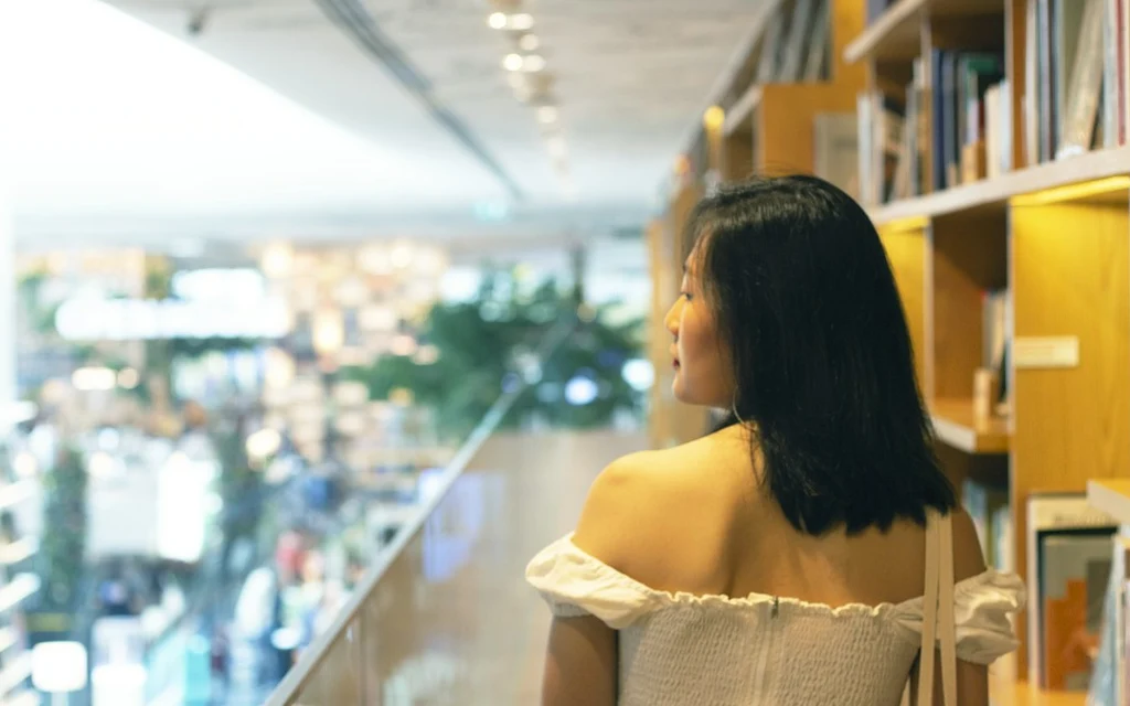woman in white off shoulder dress standing near glass wall
