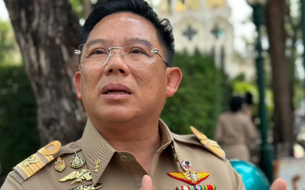 A uniformed Thai official speaking outdoors, with trees in the background.