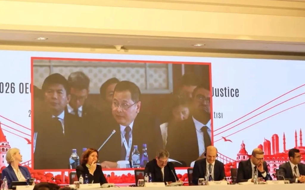 Officials attend an OECD justice meeting in Istanbul, with a speaker displayed onscreen.
