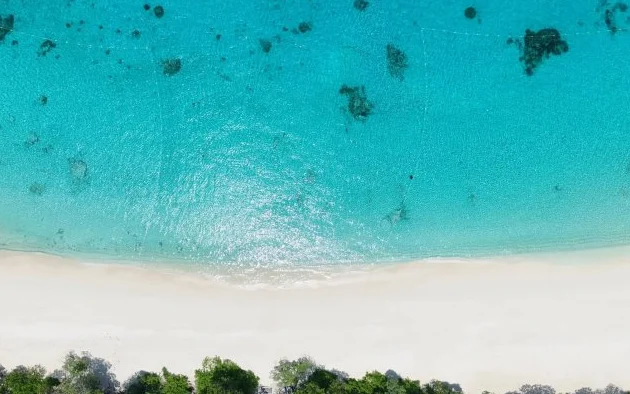 Aerial view of a white sand beach and turquoise sea.