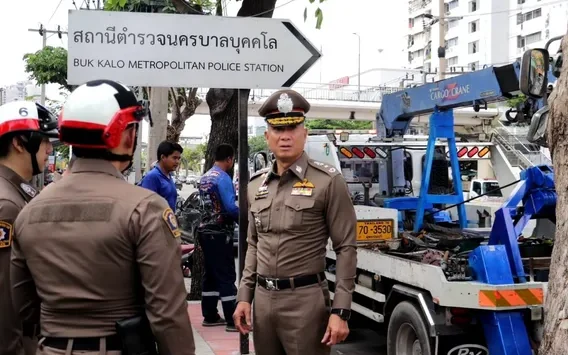 Police officers beside a truck-mounted crane near a police station sign.