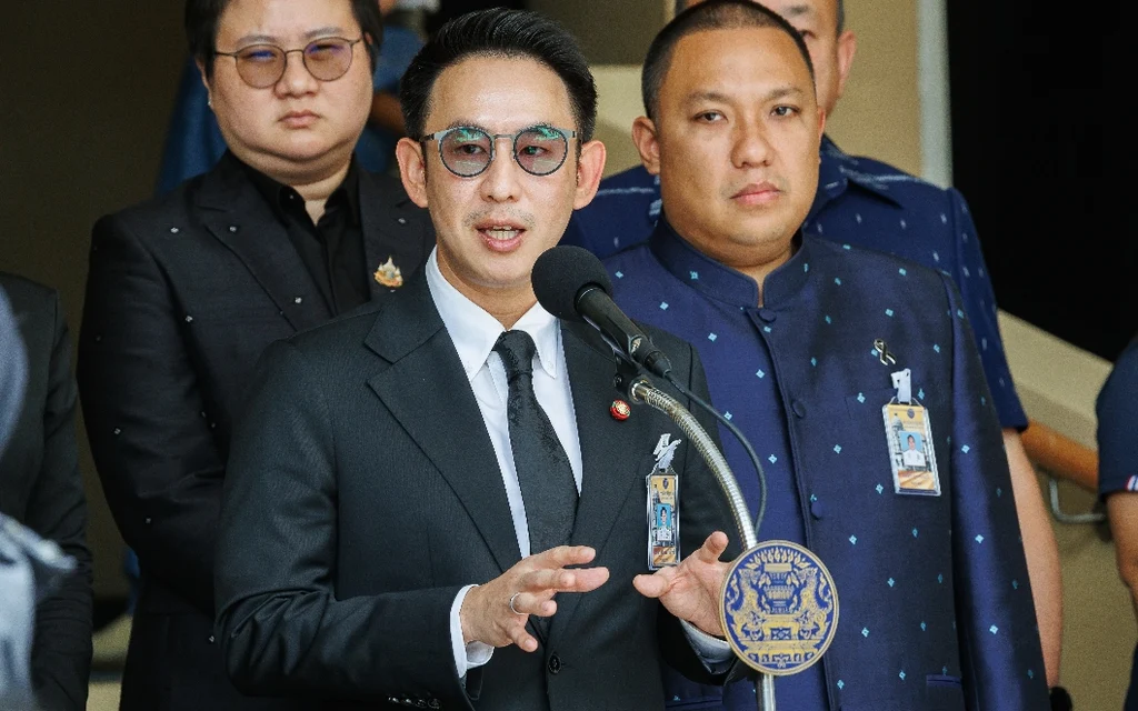 Thai official speaking at a press conference with microphones.