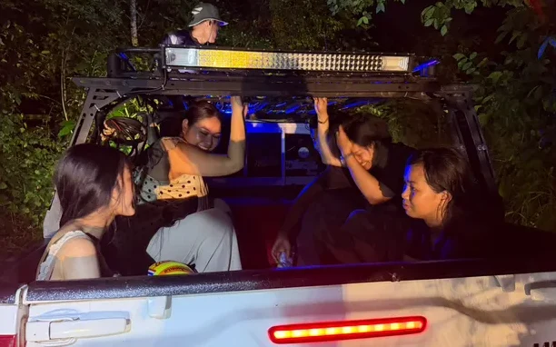 Tourists ride in the back of a pickup truck at night.