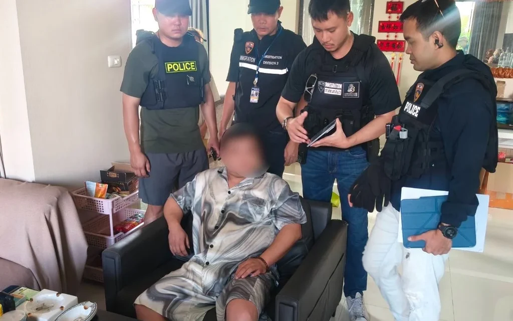 Police officers standing around a seated suspect with a blurred face in a living room.