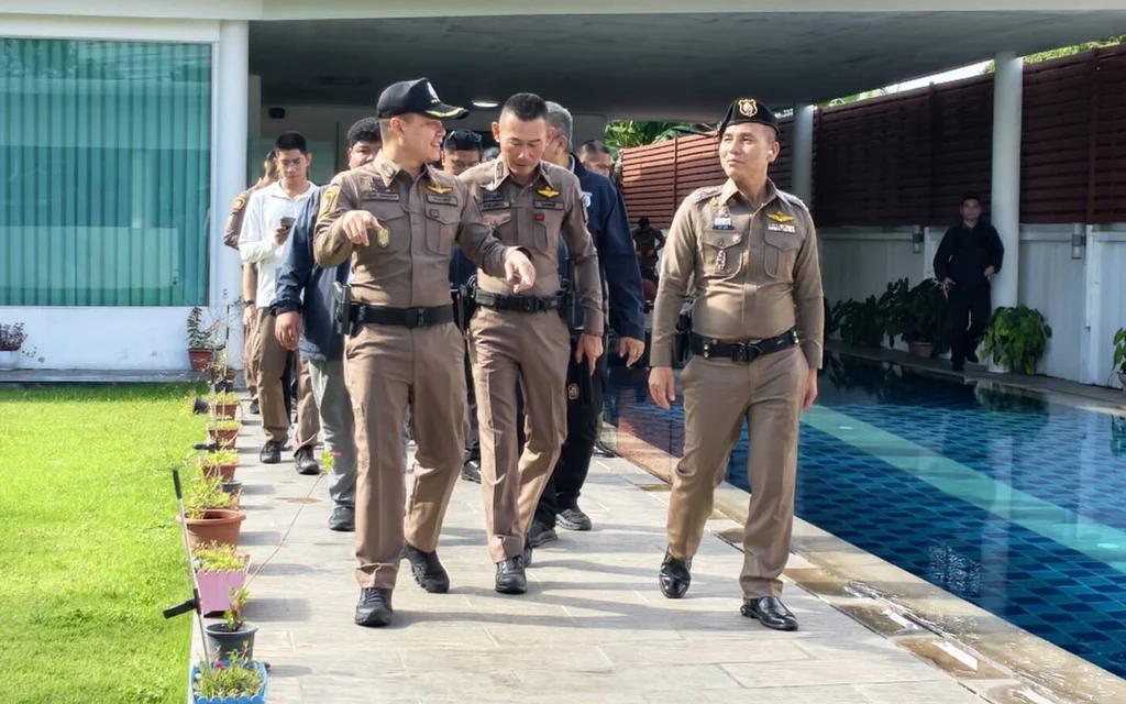 Police officers walk beside a swimming pool during a property raid.