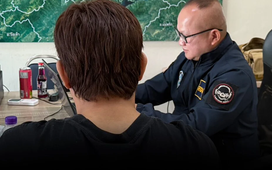 A man speaks with a uniformed officer in an office.