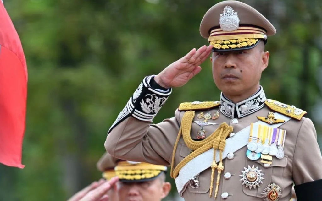 Police officers in uniform salute beside a national flag.