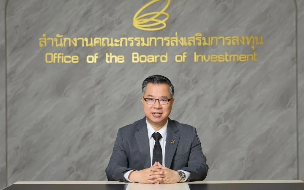 A suited official sits at a desk beneath the Board of Investment sign.