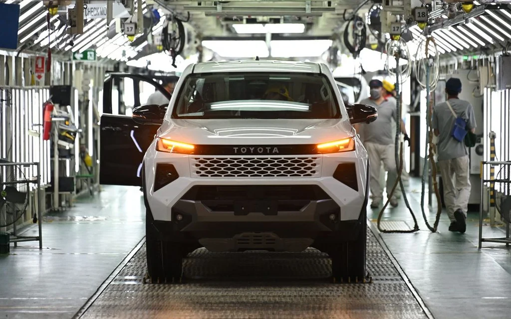 A Toyota pickup truck on an automotive assembly line with workers nearby.