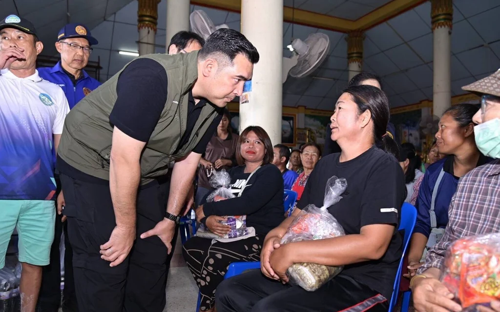 Officials speak with seated residents and distribute aid packages indoors.