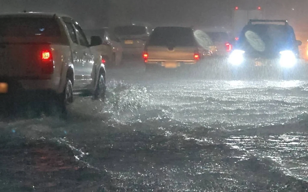 Cars driving through flooded road at night during heavy rain.