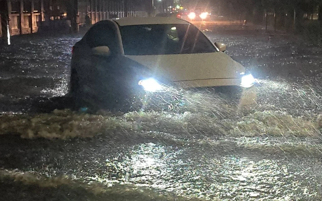 A car driving through a flooded street at night.