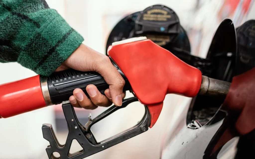 A person holds a red fuel nozzle at a gas pump.