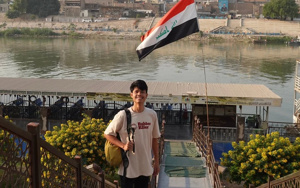 A young man standing on stairs with an Iraqi flag.