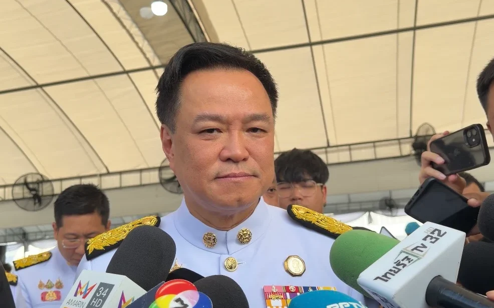 Thai politician speaks to reporters surrounded by microphones.