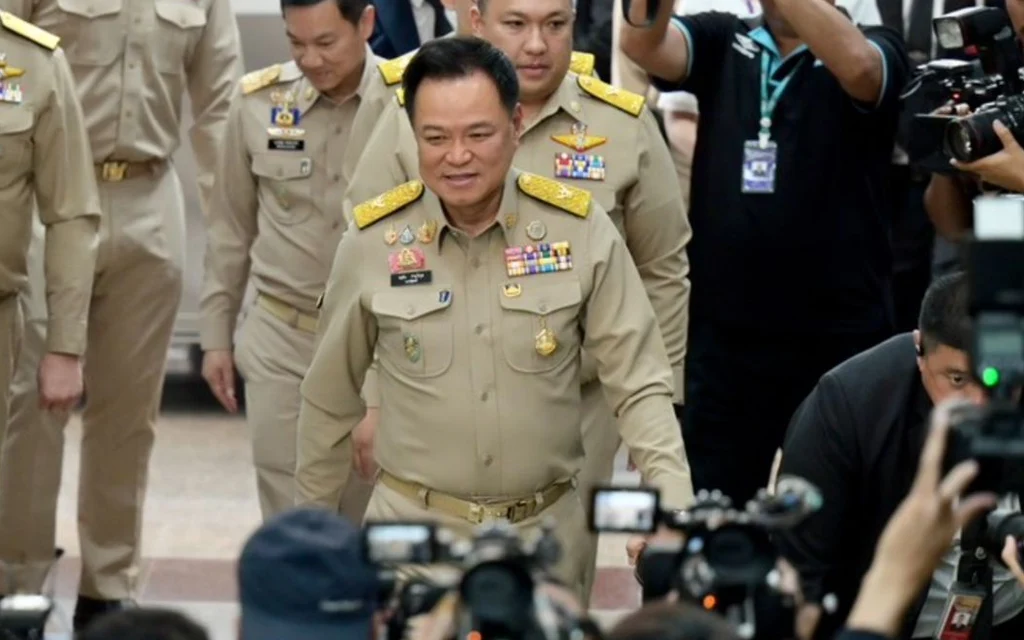 Thai officials in uniform walk past gathered photographers and media
