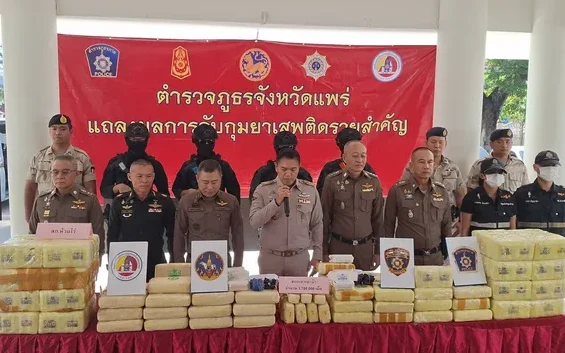 Thai police officers standing behind a table with seized drug packages.