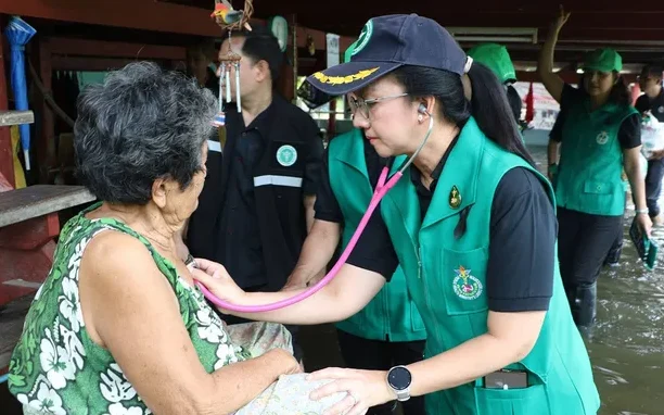 Health worker examines an elderly woman in a flooded area.