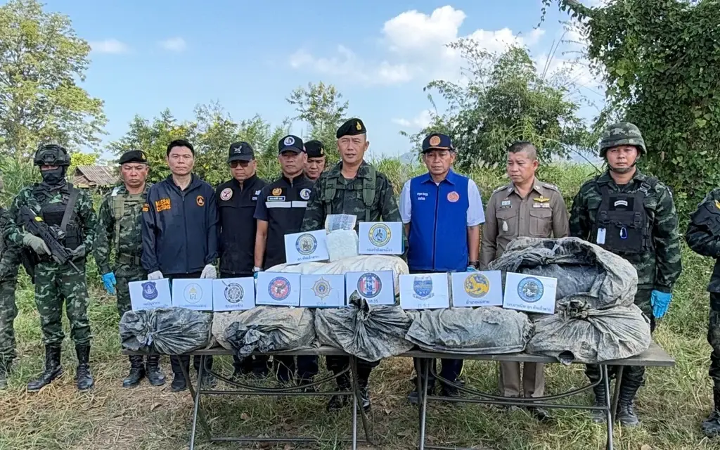 Officials and armed soldiers display seized drug packages in a field.