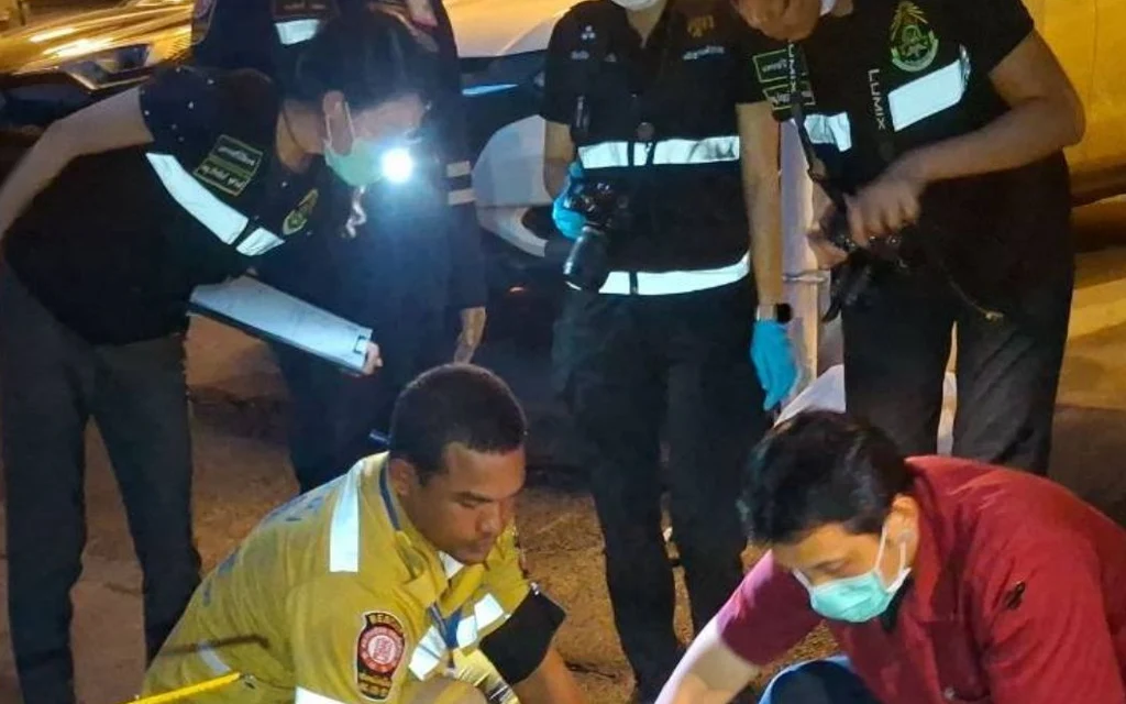 Emergency responders inspect the scene near parked vehicles at night.