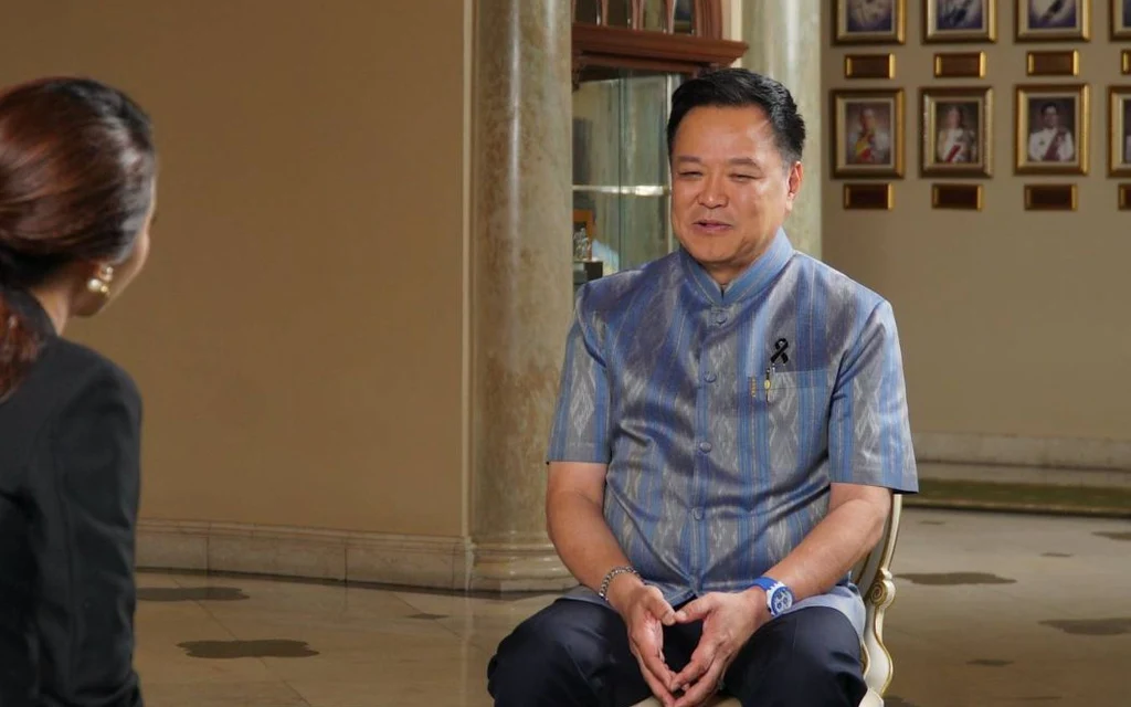 A man in blue traditional clothing sits during an interview with a woman.