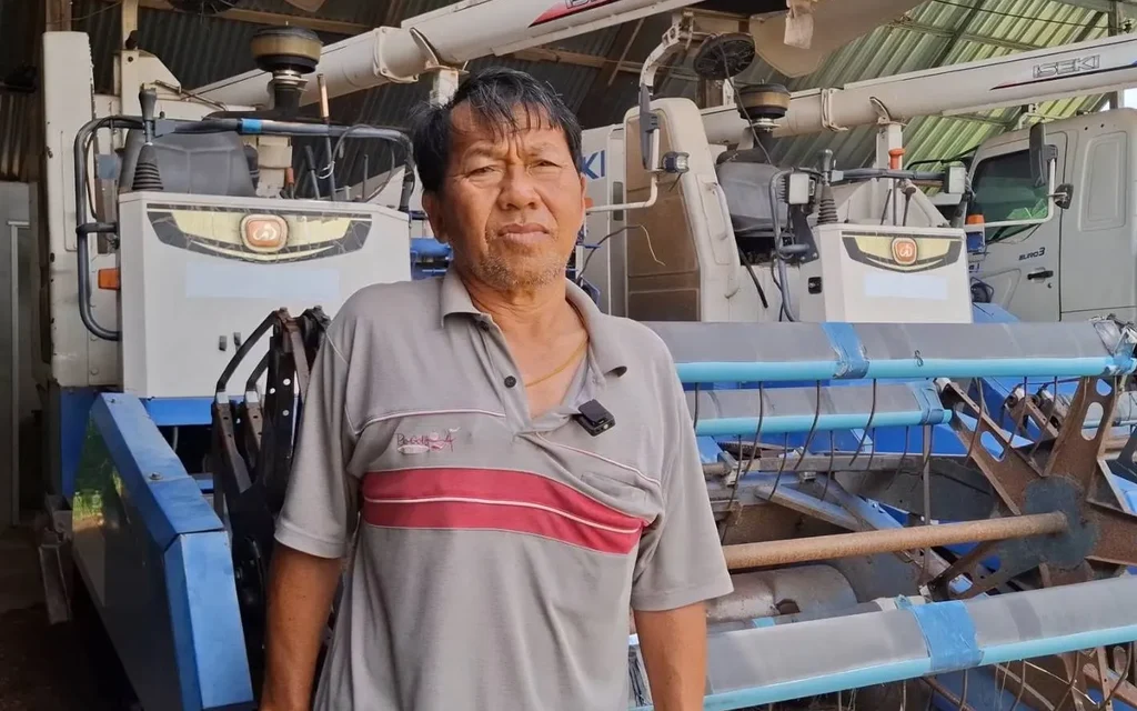 A Thai farmer standing in front of agricultural machinery.