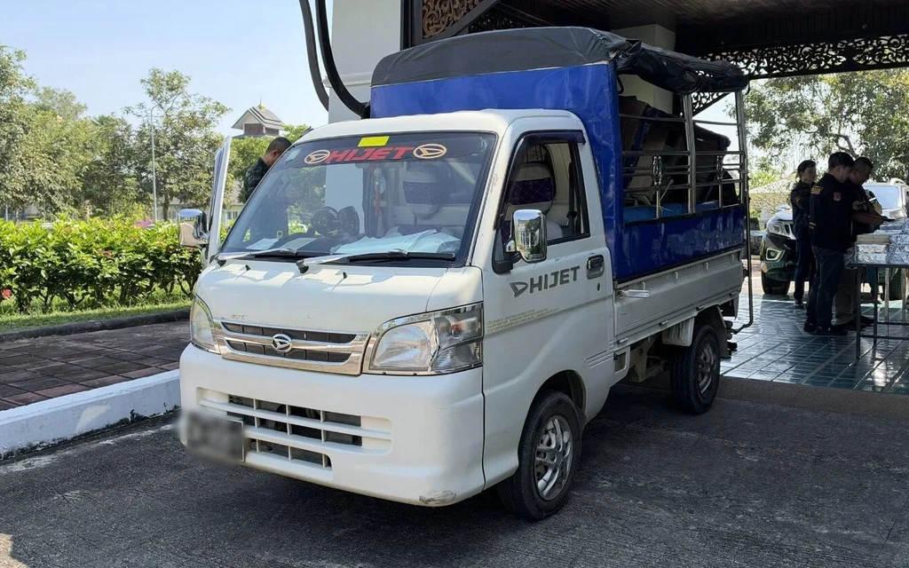 A covered pickup truck parked beside officials and tables of seized goods.