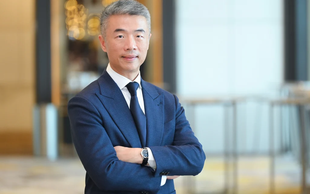 Man in a blue suit standing with arms crossed in a modern lobby