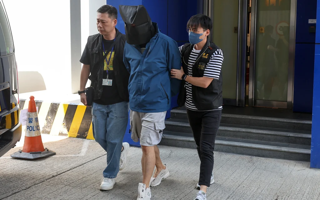 Police officers escorting a suspect with a covered head.