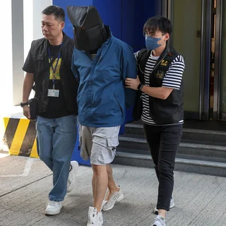 Police officers escorting a suspect with a covered head.