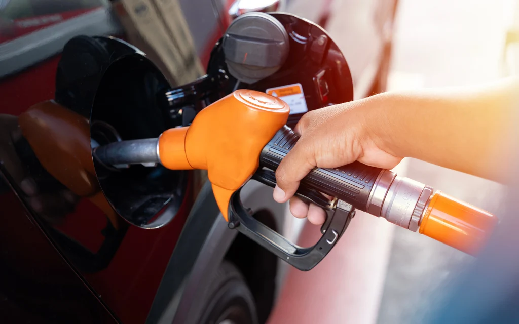 Hand refuels a car with an orange gas pump nozzle.