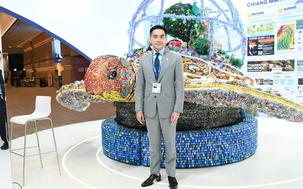 Man stands beside a recycled-material turtle display at a climate exhibition.