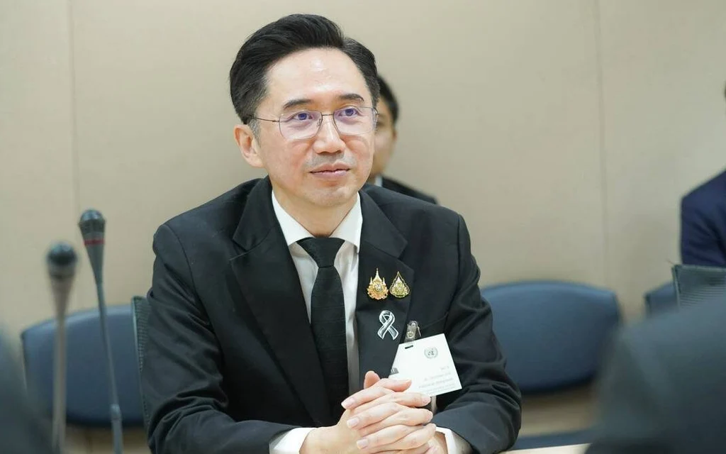 Man in a suit seated at a meeting table with microphones.