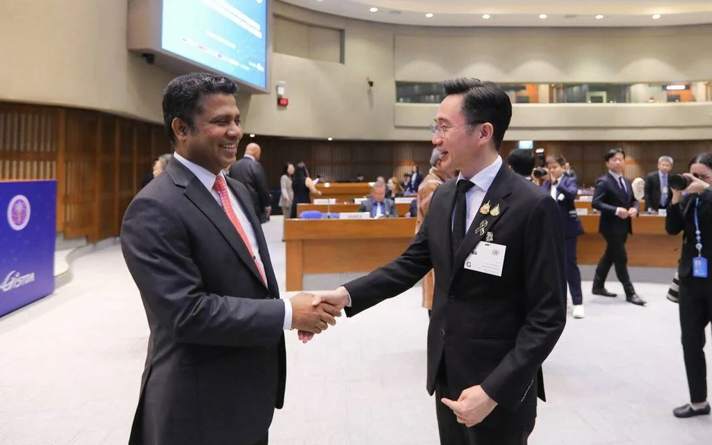 Two officials shake hands at an international conference venue.