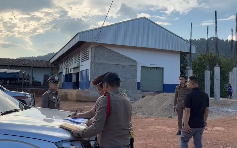 Police officers examine a car at a construction site near a school.