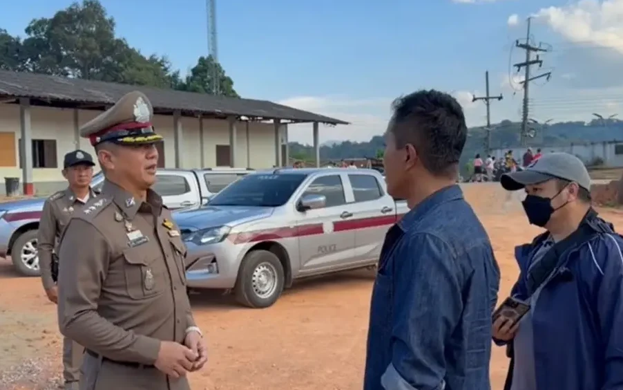 Police officer speaks with two men beside parked vehicles outdoors.