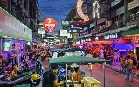 Busy Pattaya nightlife street lined with bars, signs, pedestrians, and parked motorbikes.